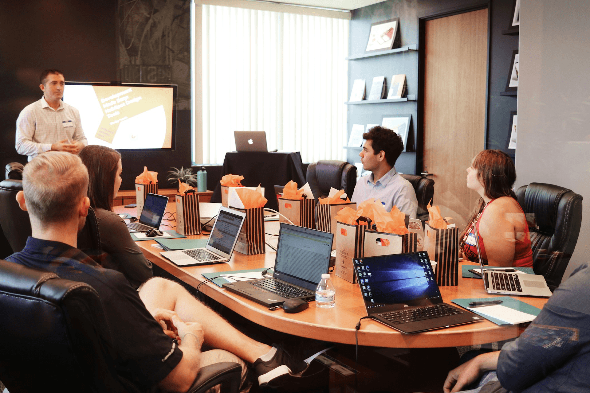 An instructor presenting to a group of professionals with laptops around a conference table